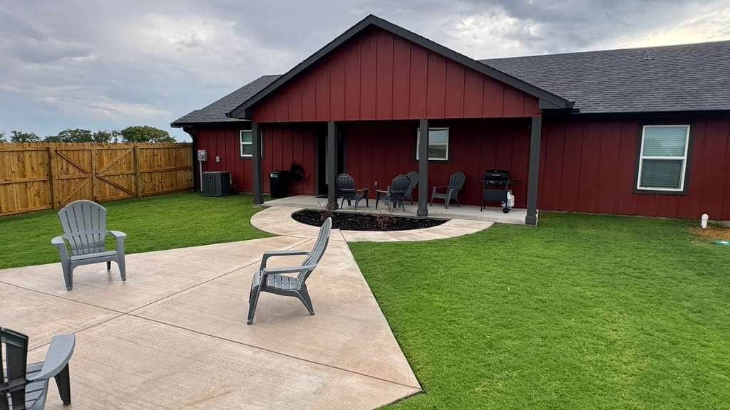 A red building with a covered patio area, a concrete deck, and a well-maintained lawn.