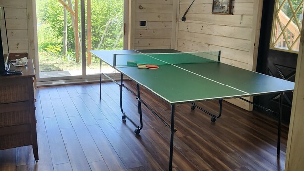 Une table de ping-pong dans une pièce au plancher en bois et dotée d’une grande fenêtre.