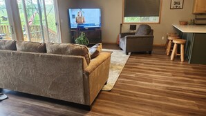 Un salon avec un canapé, un téléviseur, une petite plante et un plancher en bois.