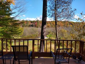 A wooden deck with two chairs and a bench, overlooking a river and autumn foliage.