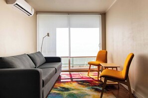 A small living area with a sofa, a chair, a colorful rug, and a large window with a view. - Bright suite with a view of Cerro Santa Lucía, one block from the Santiago Metro (Santiago)