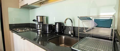 Una cocina con un lavamanos de acero inoxidable, una cafetera, un hervidor y un escurreplatos.