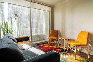 A modern living room with a sofa, two chairs, a small table, and a large window with blinds. - Bright suite with a view of Cerro Santa Lucía, one block from the Santiago Metro (Santiago)