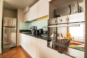 A modern kitchen with stainless steel appliances, a black countertop, and a dining area with a chair and table. - Bright suite with a view of Cerro Santa Lucía, one block from the Santiago Metro (Santiago)