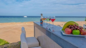 A beachside bar with a view of the ocean, a boat in the distance, and a tray of fruits and drinks.