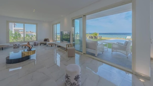 A spacious living room with a large glass door leading to a balcony with a view of the sea.