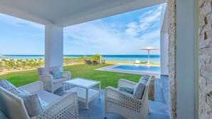 A covered outdoor seating area with wicker furniture, a pool, and a view of the ocean.