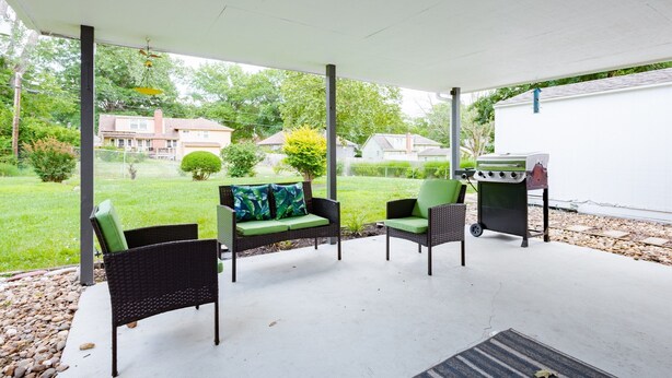 An outdoor patio with wicker furniture, a grill, and a view of a residential area.
