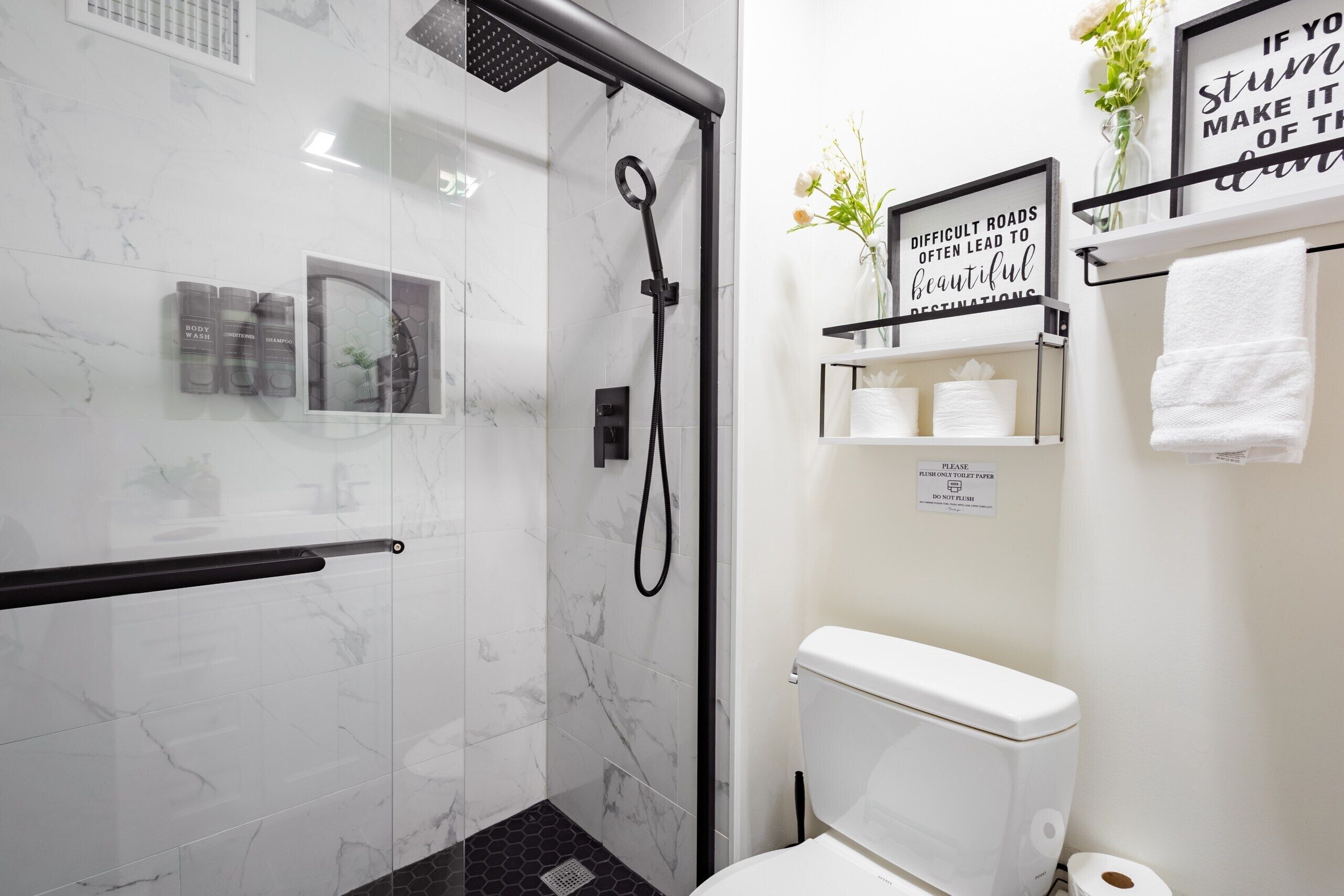 Un baño moderno con ducha, inodoro y un estante con artículos de aseo.