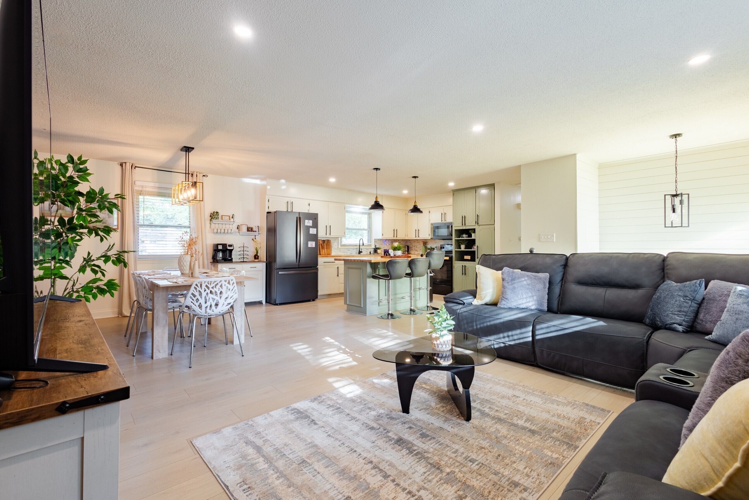 A modern living room with a black leather sofa, a coffee table, and a dining area with a wooden table and chairs.