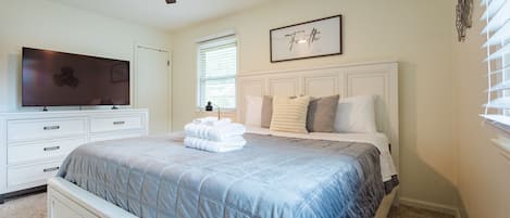 A bedroom with a bed, a television, a ceiling fan, and a framed quote on the wall.