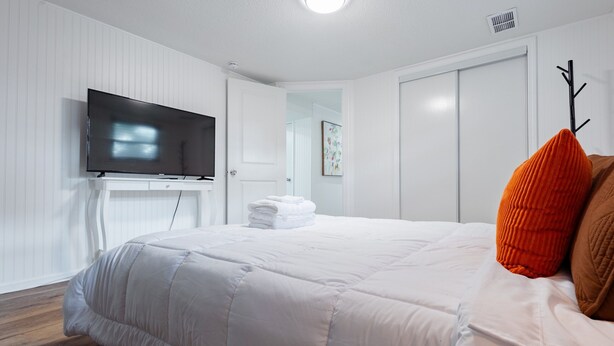Ett hotellrum med en stor säng, en platt-TV som är monterad på väggen och en dörr som leder till badrummet.