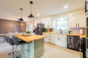 A modern kitchen with a wooden island, bar stools, a refrigerator, and a dishwasher. - Fully Furnished 4-Bedroom,All Utilities Included, Perfect for Insurance Housing (Grandview)
