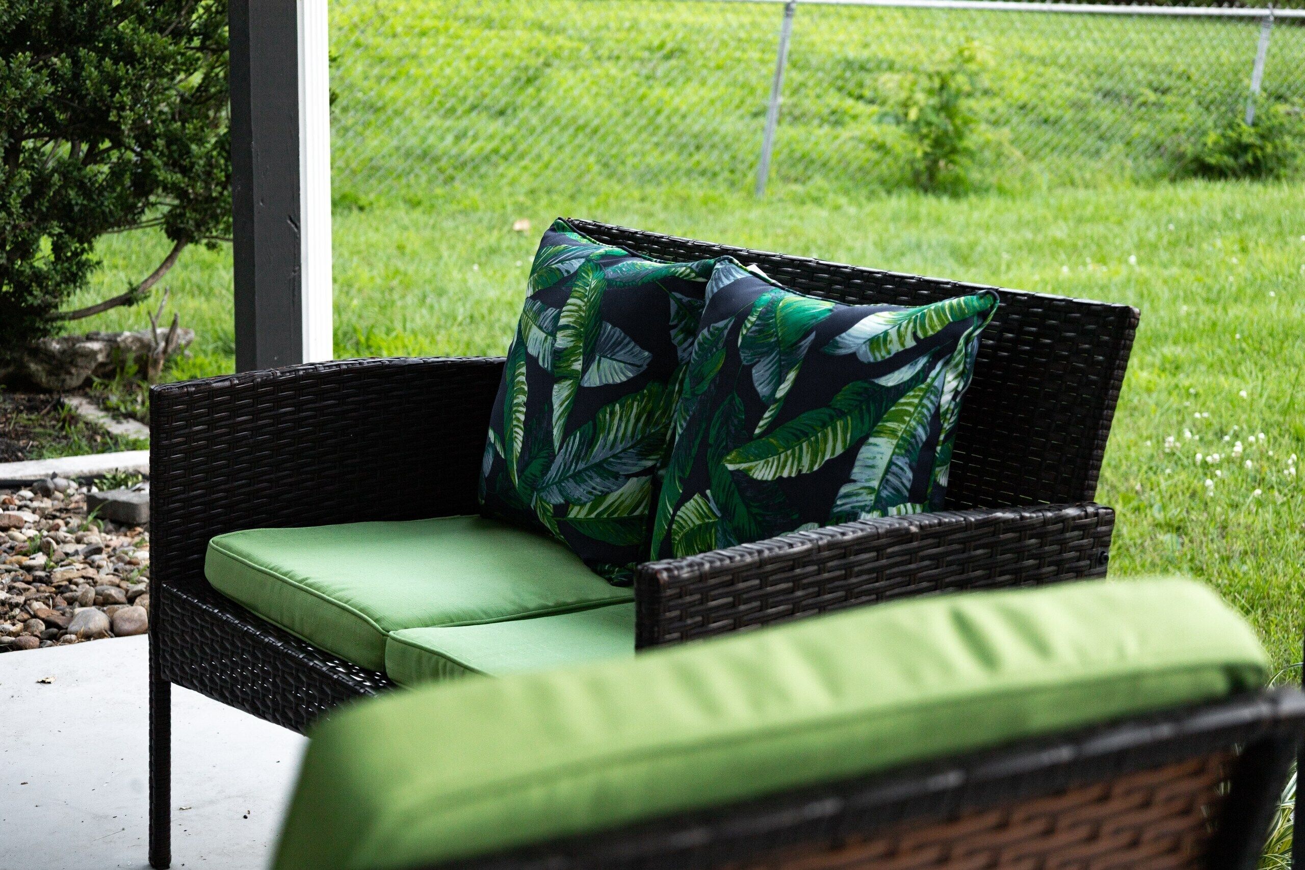 A wicker outdoor seating area with a green cushion and a leaf-patterned pillow.