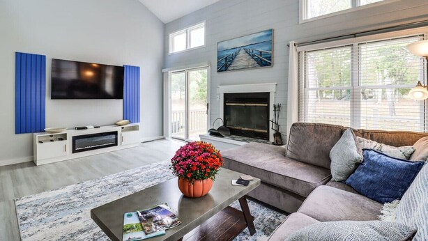 A living room with a flat-screen TV, a fireplace, a sofa, and a coffee table with flowers. - Pocono Mountains Gem (East Stroudsburg)