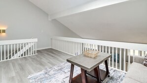 A spacious attic room with a sloped ceiling, a wooden table with a glass bowl, and a white railing. - Pocono Mountains Gem (East Stroudsburg)
