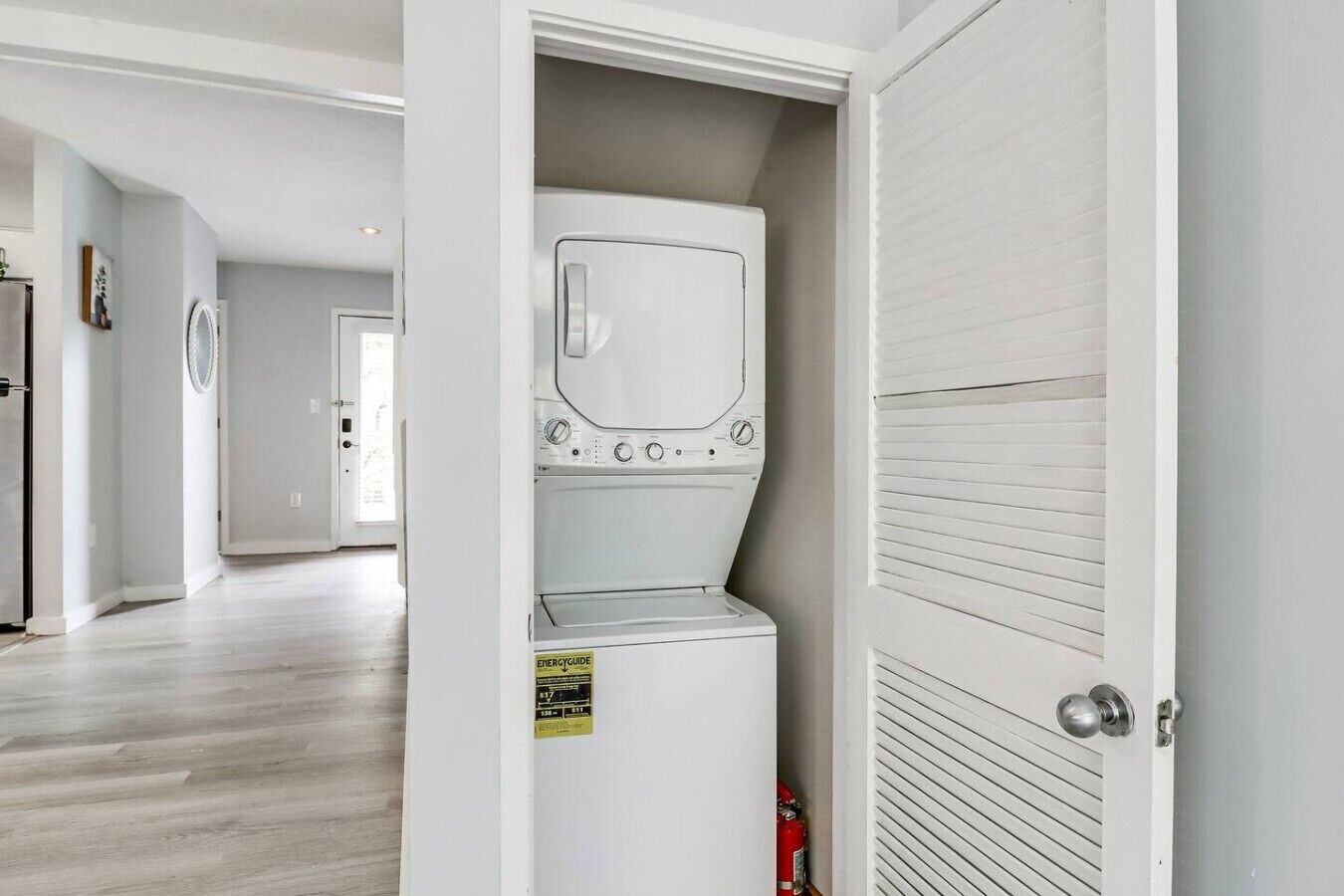 A laundry room with a washer and dryer, a fire extinguisher, and a door leading to another room.