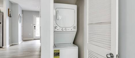 A laundry room with a washer and dryer, a fire extinguisher, and a door leading to another room.