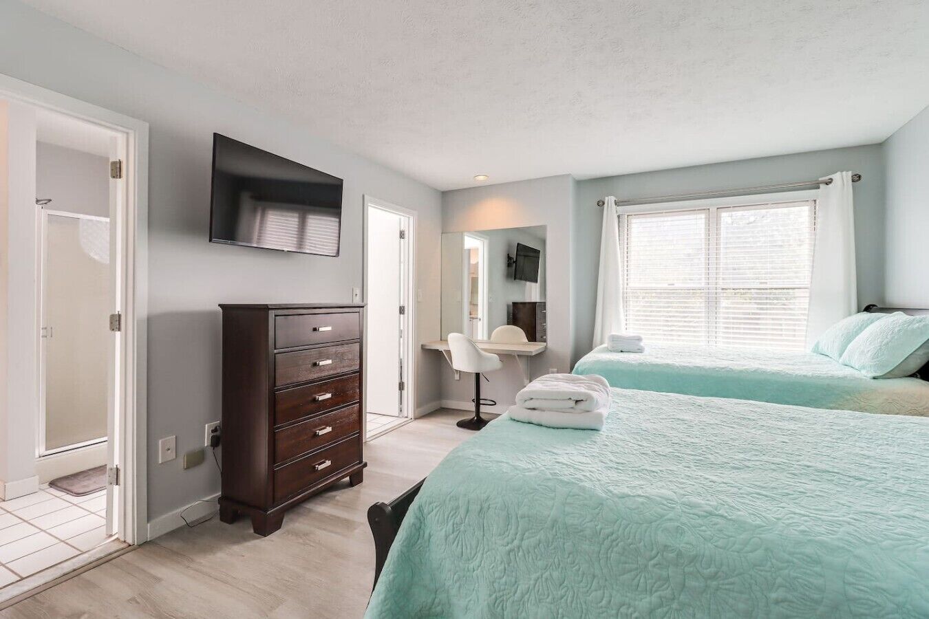 A bedroom with two beds, a dresser, a desk, and a television.