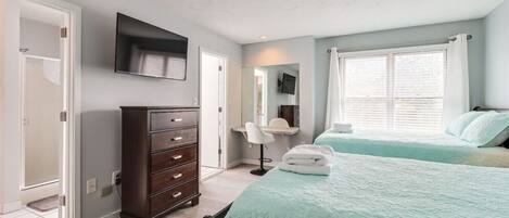 A bedroom with two beds, a dresser, a desk, and a television.