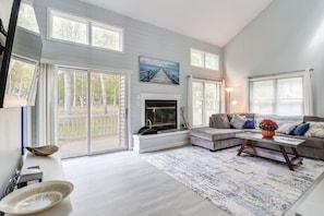 A spacious living room with a fireplace, a sofa set, and a large window overlooking a deck.