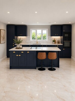 A modern kitchen with dark cabinetry, a marble countertop, and a central island with stools. - Luxury Modern House in Mid Devon (Crediton)
