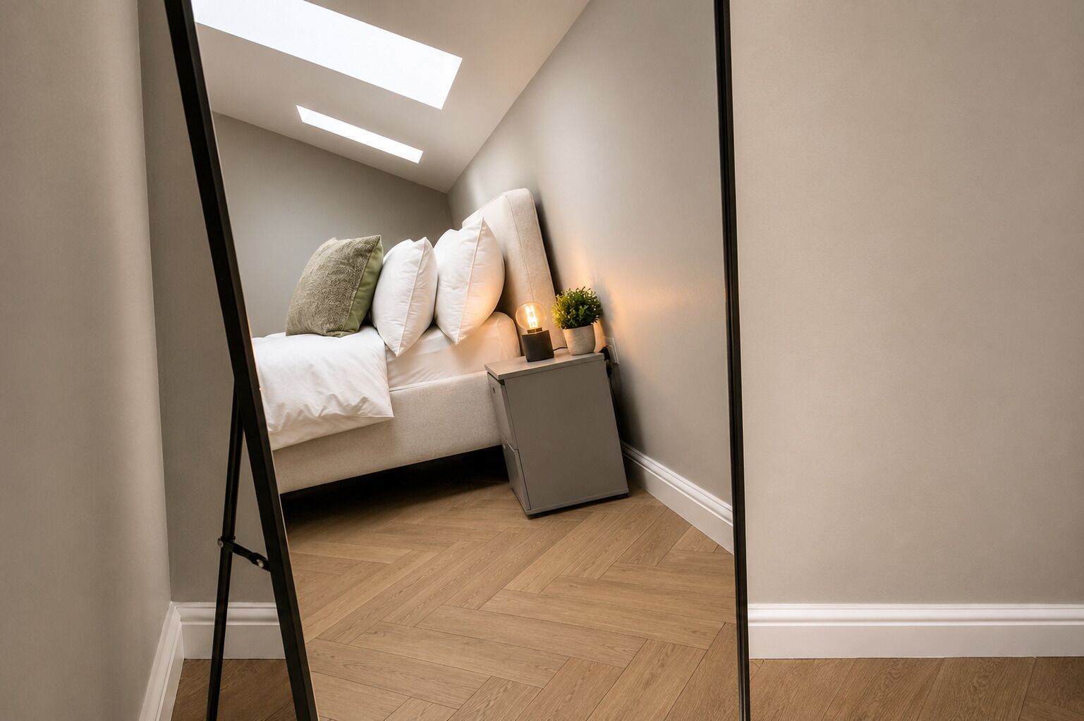A bedroom with a bed, pillows, a nightstand with a lamp, a small plant, and a radiator.