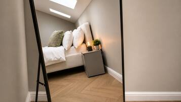 A bedroom with a bed, pillows, a nightstand with a lamp, a small plant, and a radiator.