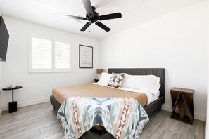 A bedroom with a bed, a ceiling fan, a window with blinds, a framed picture on the wall, and a small table. - Scottsdale Oasis with Heated Pool, Putting Green & Fire Pit (Scottsdale)
