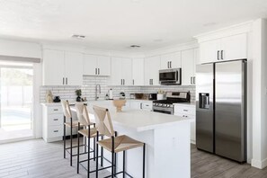 A modern kitchen with white cabinetry, a stainless steel refrigerator, and a central island with bar stools. - Scottsdale Oasis with Heated Pool, Putting Green & Fire Pit (Scottsdale)