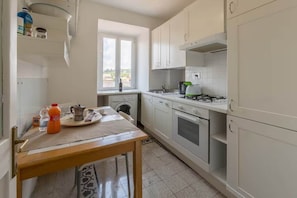 A kitchen with white cabinets, a gas stove, a sink, and a window. - Campo de' Fiori | Panoramic View & 2 Bedrooms (Rome)