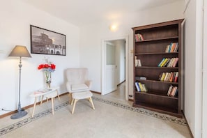 A room with a bookshelf, a chair, a small table with a lamp, and a framed picture on the wall. - Campo de' Fiori | Panoramic View & 2 Bedrooms (Rome)
