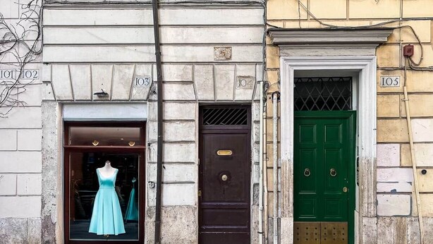 A building facade with numbered doors, a mannequin in a dress, and a green door. - Campo de' Fiori | Private Rooftop Terrace (Rome)