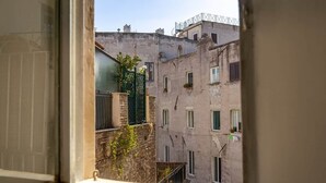A view through a window of a multi-story building with balconies and a green gate. - Campo de' Fiori | Private Rooftop Terrace (Rome)
