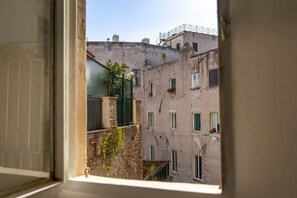 Blick durch ein Fenster auf ein mehrgeschossiges Gebäude mit Balkonen und einem grünen Tor.