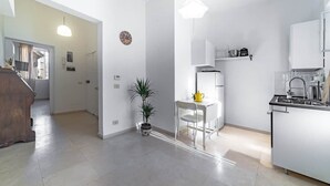 A modern kitchen with white cabinetry, a central island, and a dining area with a chair and table. - Campo de' Fiori | Private Rooftop Terrace (Rome)