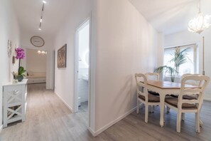 A modern interior with a dining area featuring a wooden table and chairs, a white console table with a vase, and a hallway leading to a bathroom. - Vatican Shabby double bedrooms (Rome)