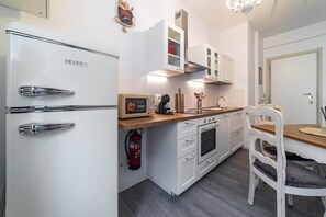 A compact kitchen with white cabinetry, a built-in oven, a sink, and a dining area with a wooden table and white chairs. - Vatican Shabby double bedrooms (Rome)