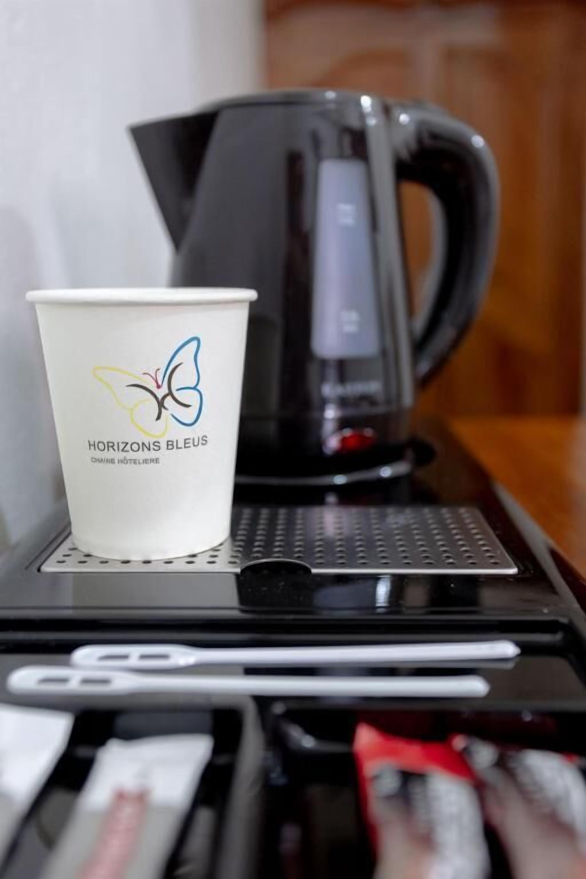 Una taza de café con un logotipo, una cafetera de café negro y un teléfono inteligente sobre una mesa.
