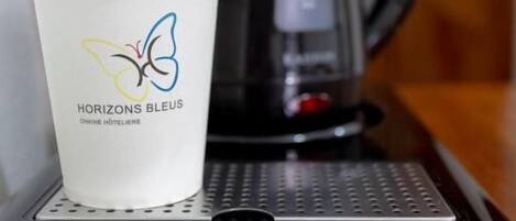 A coffee cup with a logo, a black coffee pot, and a smartphone on a table.