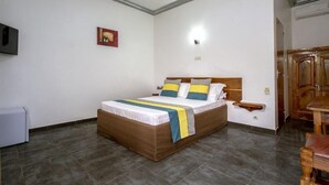 A bedroom with a bed, a bedside table, a TV mounted on the wall, and a wooden cabinet. - Le relais de Kolda  (Kolda)