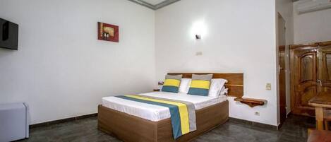 A bedroom with a bed, a bedside table, a TV mounted on the wall, and a wooden cabinet.