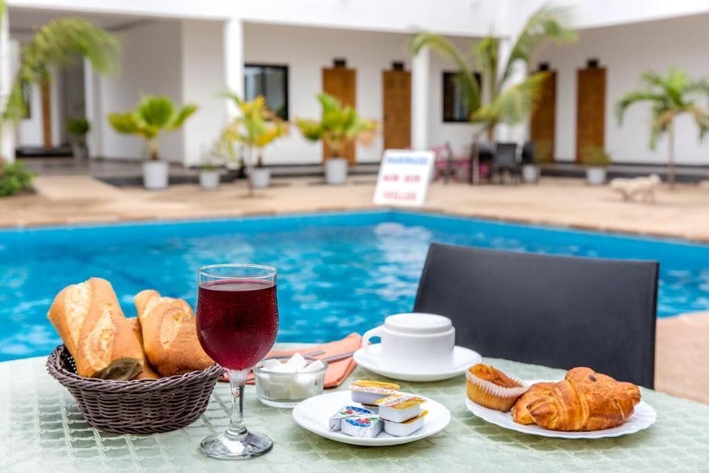 Et spisebord med brød, et glas rød drik, en kop og kager ved en pool.