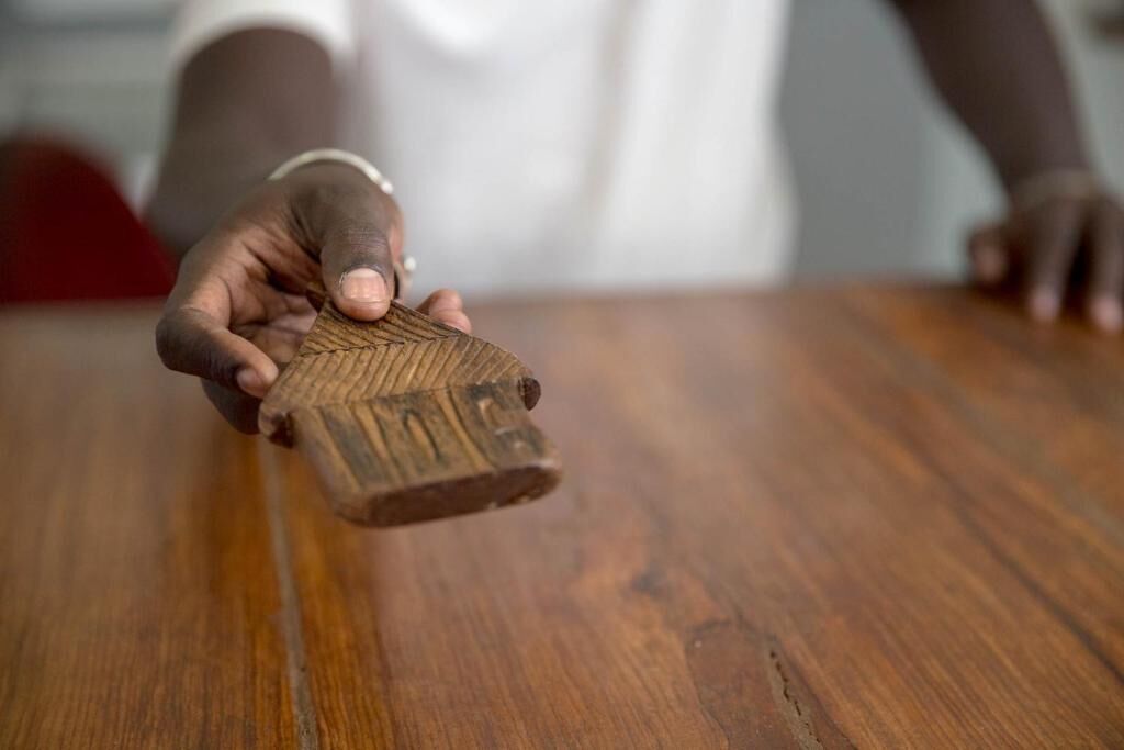 A person holding a wooden object with a textured surface and a circular indentation at the top.
