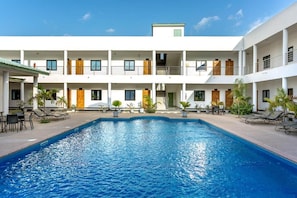 Un hotel con piscina central, varios balcones y zonas de estar al aire libre.