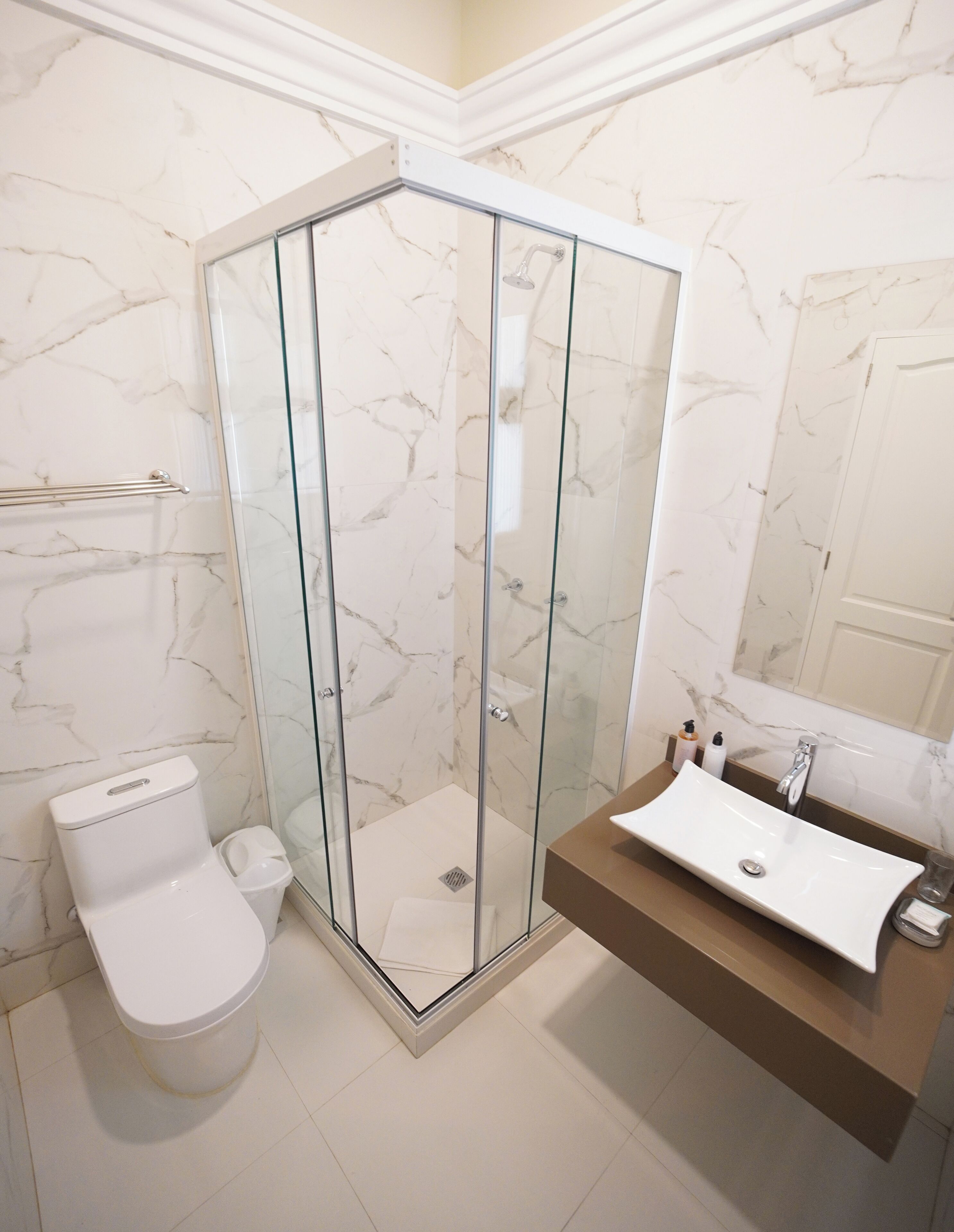 A modern bathroom with a glass-enclosed shower, a white toilet, and a sink with a marble countertop.