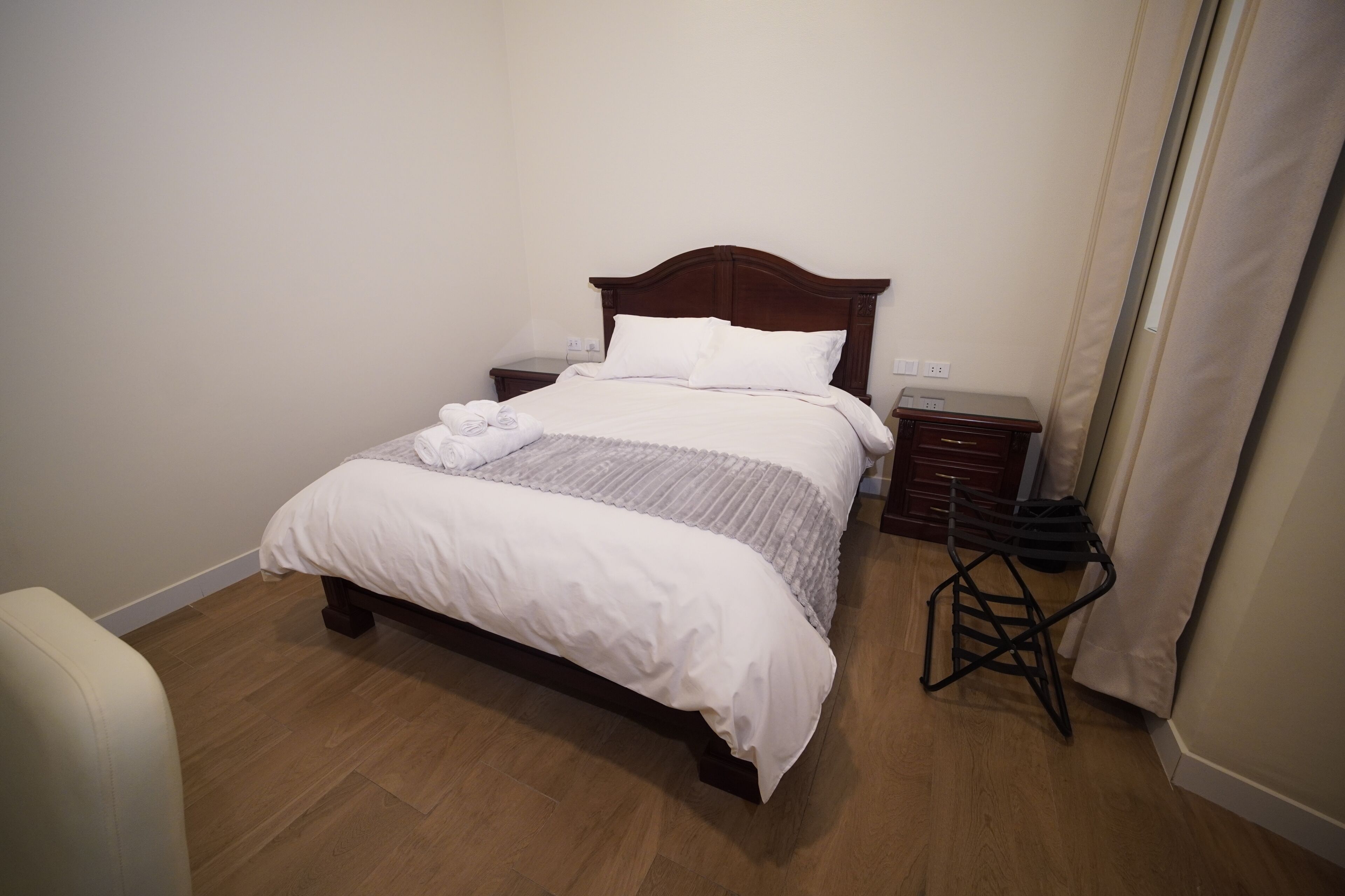 A neatly made bed with a wooden headboard, a bedside table, and a small stool.