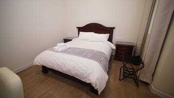 A neatly made bed with a wooden headboard, a bedside table, and a small stool.
