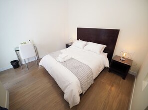 A neatly made bed with white linens, a dark headboard, and a bedside table with a lamp.