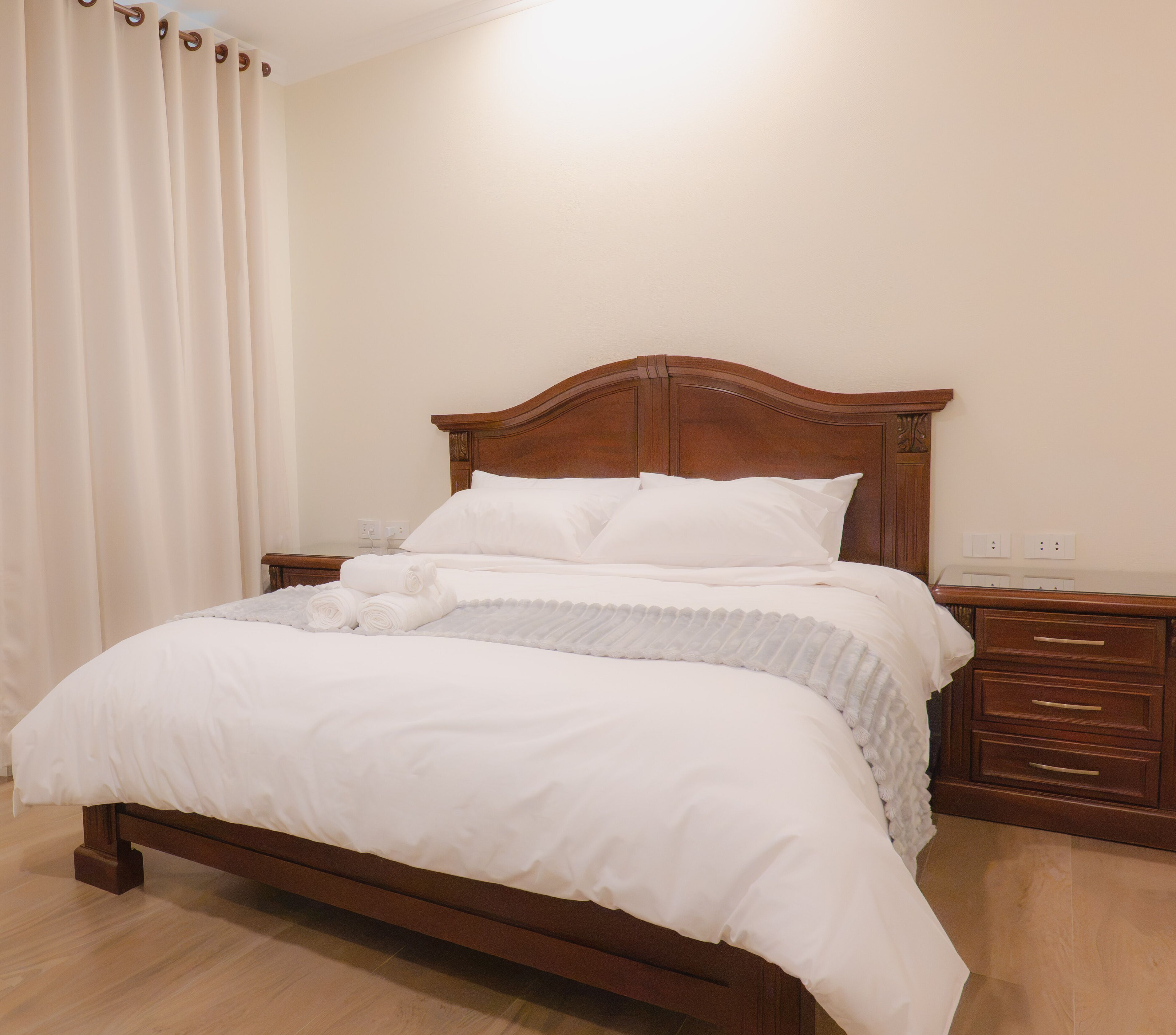 A neatly made bed with white bedding, a wooden headboard, and a bedside table with drawers.